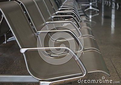 A row of metal chrome grey shiny seats on the floor of large tiles imitating marble in the airport , selective focus. Stock Photo