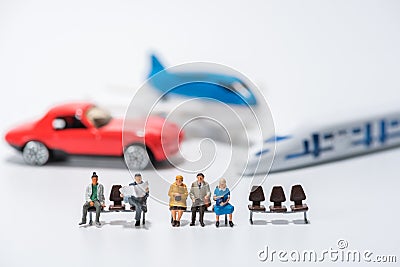 row of miniature people figure sitting on bench with air plane,car,hispeed train model figure background Stock Photo