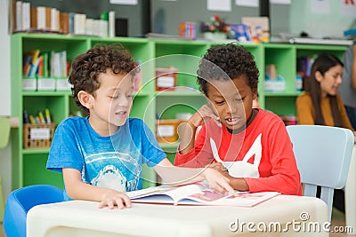 Row of multiethnic elementary students reading book in classroom. Stock Photo