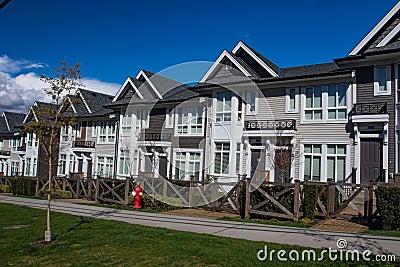 Row of new townhomes in a sidewalk neighborhood. On a sunny day in spring against bright blue sky. Stock Photo