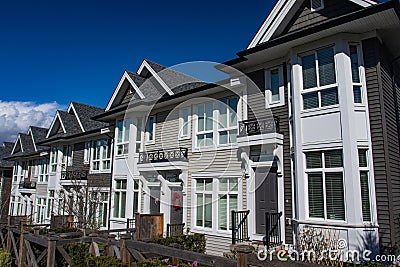 Row of new townhomes in a sidewalk neighborhood. On a sunny day in spring against bright blue sky. Stock Photo