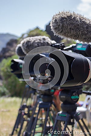 Row of professional video cameras outdoor. Camera with microphone on tripod. TV reality show filming. News and reportage concept. Stock Photo