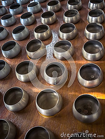 Row of silvery alms bowls with little coins inside in buddhist temple Stock Photo