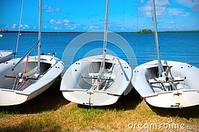 Row of small sailboats lined up along the coast shoreline used for teaching sailing Stock Photo