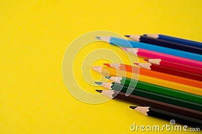 A row of unevenly arranged colored pencils on a yellow background with copy space Stock Photo
