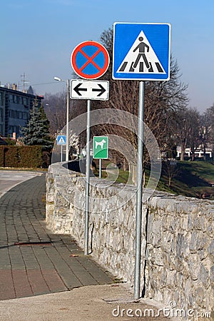 Row of various road signs from pedestrians crossing to no stopping or parking road sign and dogs allowed sign next to stone wall Stock Photo