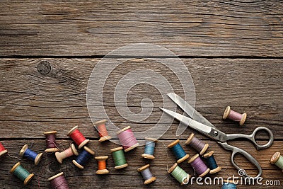Row of vintage wooden spools of multicolored threads, tailoring scissors, sewing items on wooden board. Stock Photo