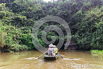 Rowing woman row a boat with tourist on the river with cave entrance in the background at Trang An Grottoes in Ninh Binh, Vietnam Editorial Stock Photo