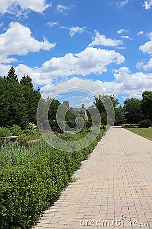 Rows of shrubbery and flowers lining a brick walkway leading to a cottage on a summer day in Boerner Botanical Gardens Editorial Stock Photo