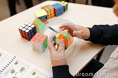 Rubik`s cube in children`s hands, closeup, white wooden background. Boy holding Rubik`s cube and playing with it Editorial Stock Photo