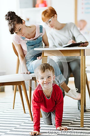 Rude kid sitting under the table during therapy for ADHD with his mother and professional therapist Stock Photo