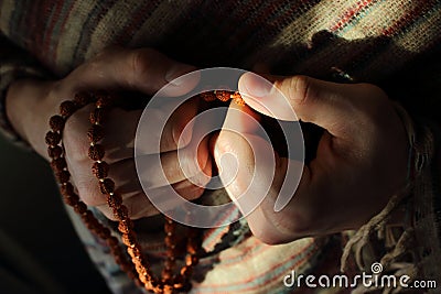 Rudraksha beads in men`s hands in traditional indian shawl. Man counting religious beads in sunlight. Stock Photo