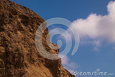 Rugged jagged brown cliff edge with a seagull on a ledge. Deep blue sky background with broken puffy clouds Stock Photo