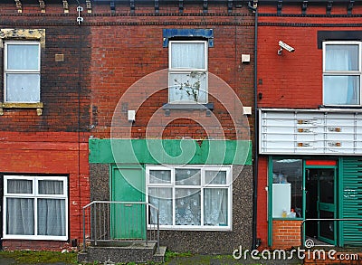 Run down terraced houses on a street in leeds with shabby decaying colourful painted walls and a shop front with an open door Stock Photo