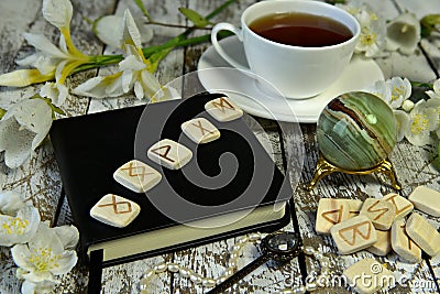 Runes on black diary book, crystal and cup of tea on witch table Stock Photo