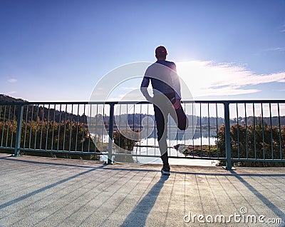 Runner doing stretching exercise on bridge. An active wiry man Stock Photo