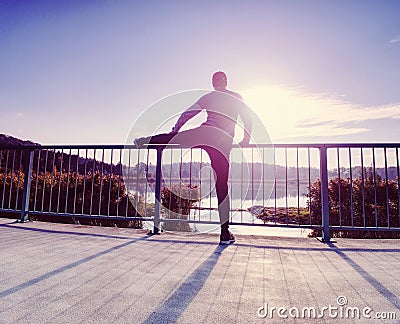 Runner doing stretching exercise on bridge. An active wiry man Stock Photo