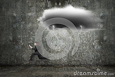 Running businessman holding tablet with dark clouds raining and Stock Photo