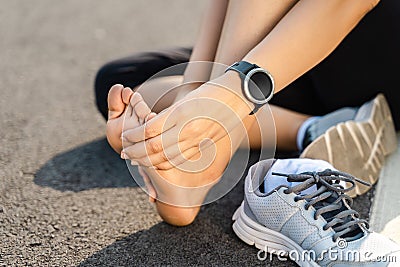 Running injury leg accident- sport woman runner hurting holding painful sprained ankle in pain. Female athlete with joint or Stock Photo