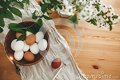 Rural Easter flat lay. Natural eggs in wooden bowl and vintage candle on linen fabric on background of cherry flowers and green Stock Photo