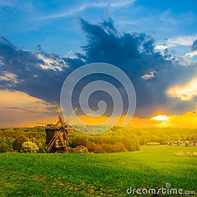 Rural ethnic landscape, green fields with wooden windmill at the sunset Stock Photo