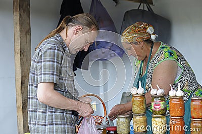 Rural food market. Man buying food from middle aged woman street seller, cans with pickles on a foreground. Klavdiivka Editorial Stock Photo