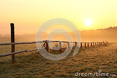 rural landscape at sunrise with wooden fence in the field in misty weather wooden fence in the field lit by rising sun in foggy Stock Photo