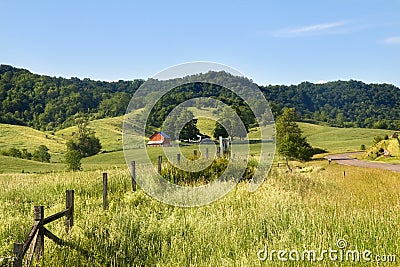 Rural pastoral landscape with meadows,wooden fence and isolated red house. Stock Photo