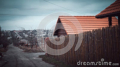 Rural street. Fence made of sharp wooden stakes. House with a red tiled roof Stock Photo
