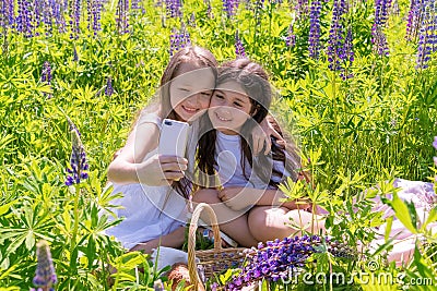 Russia, Kazan - June 7, 2019 Two baby girls make selfie on a phone among flowers in a field on a sunny day. The concept of summer Editorial Stock Photo