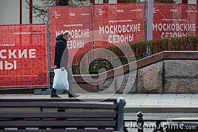 Russia, Moscow, April 2020. Empty street. A lone pedestrian in a disposable mask with bags on the background of the posters Editorial Stock Photo