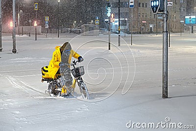 Employee, food deliverer from Yandex.Food rides an electric bike through the snow. Editorial Stock Photo