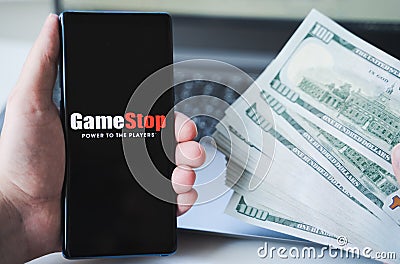 Russia Moscow 02.02.21 Mobile phone with logo of Gamestop, money, dollars in hand. Company making video games. Trading exchange, Editorial Stock Photo
