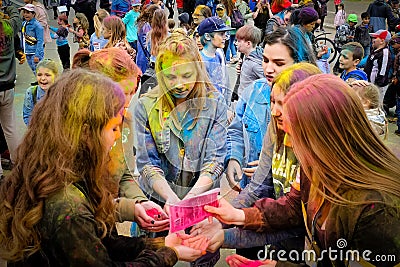 Holi Indian holiday. Young people in the crowd pour colored powder into their hands and throw it up and have fun. Faces and Editorial Stock Photo