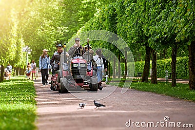 Russia, Peterhof, 16.06.2022 - A team of gardeners rides on a garden tractor in a large park. Editorial Stock Photo