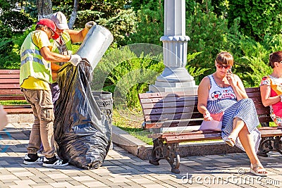 Utility workers collect garbage from an urn in a bag in a park Editorial Stock Photo