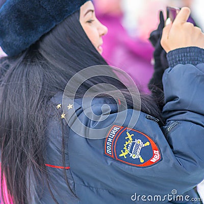 A girl in a winter Russian police uniform is looking at a smartphone. Russian text: Police MIA Editorial Stock Photo