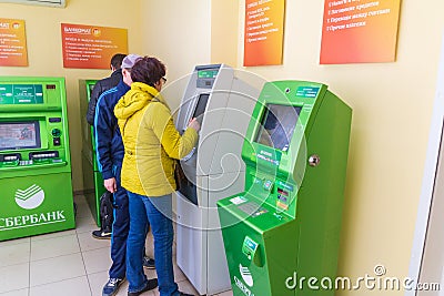 Mature beautiful woman pays utilities through an ATM. Text in Russian: Sberbank, ATM Editorial Stock Photo