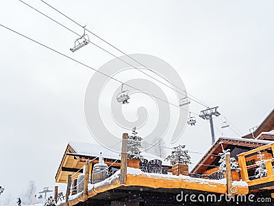 Russia, Sochi 22.01.2020. Chair lift with skiers over wooden cafe with terrace on sky background Editorial Stock Photo