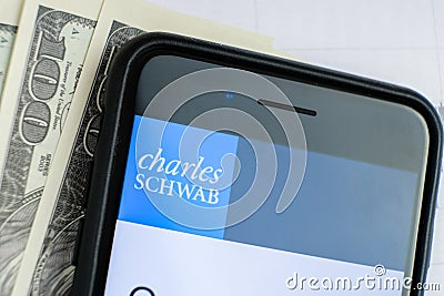 RUSSIA, ST.PETERSBURG, April 4, 2019: Logo Charles Schwab in the smartphone lying charts and dollar bills Editorial Stock Photo