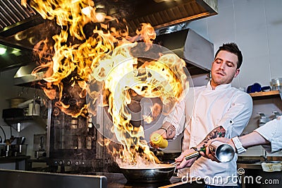 Russia, St. Petersburg, 03.17.2019 - chef is making flambe in a restaurant kitchen, dark background. Editorial Stock Photo