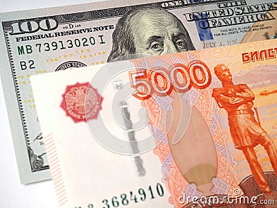 The Russian banknote of five thousand rubles hangs over the American banknote of one hundred dollars. The focus is on Franklin`s Stock Photo