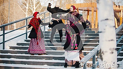 Russian folk - men and women in felt boots are dancing on the stairs in the winter park Stock Photo