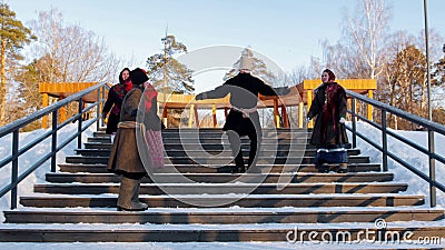 Russian folk - young people in felt boots are dancing on the stairs in the winter park Stock Photo