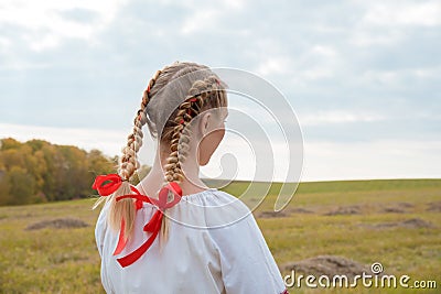 Russian girl Slavic appearance with braids with red ribbons in the field in autumn Stock Photo