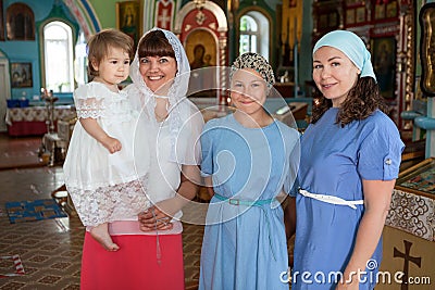 Russian women before toddler baptism are in church, godmother with goddaughter, mother with teenager daughter, indoor portrait Stock Photo