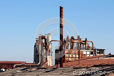 Rusted metal chimneys surrounded with large storage silos on top of destroyed rooftops at abandoned industrial complex Stock Photo