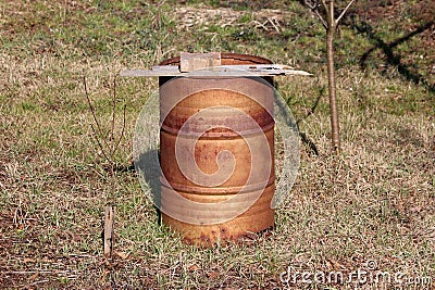 Rusted old metal oil barrel used as large garbage can for weeds and old plants with cracked wooden board and stone tile on top Stock Photo