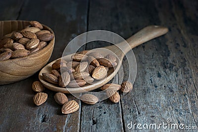 On a rustic hardwood floor, almonds in a wooden ladle and a wooden bowl Stock Photo