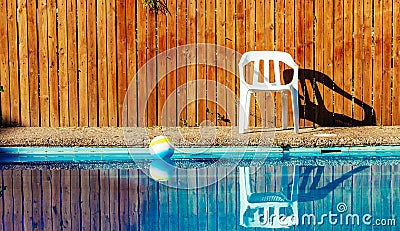 Rustic pool side space outskirts villa back yard white plastic chair and ball float water surface background view fenced by wooden Stock Photo